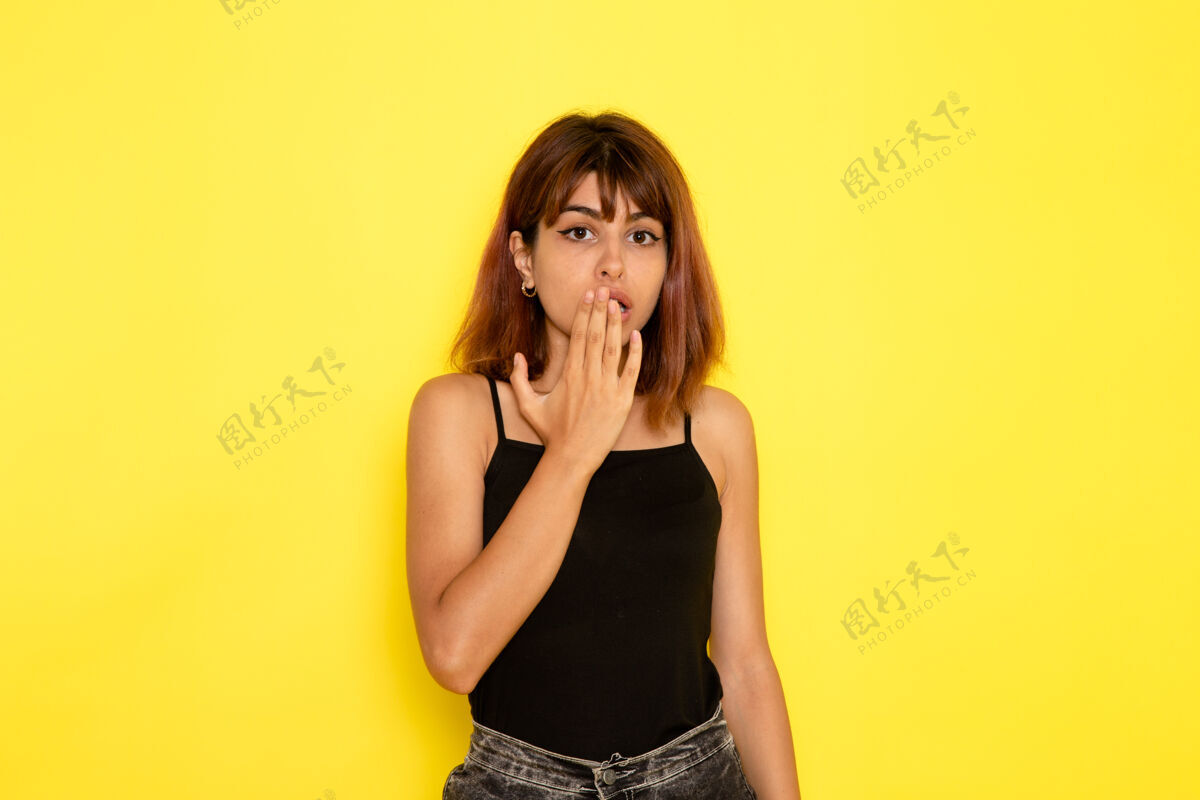 年轻身穿黑色衬衫和灰色牛仔裤的年轻女性在黄色墙壁上摆姿势的前视图头发姿势女孩