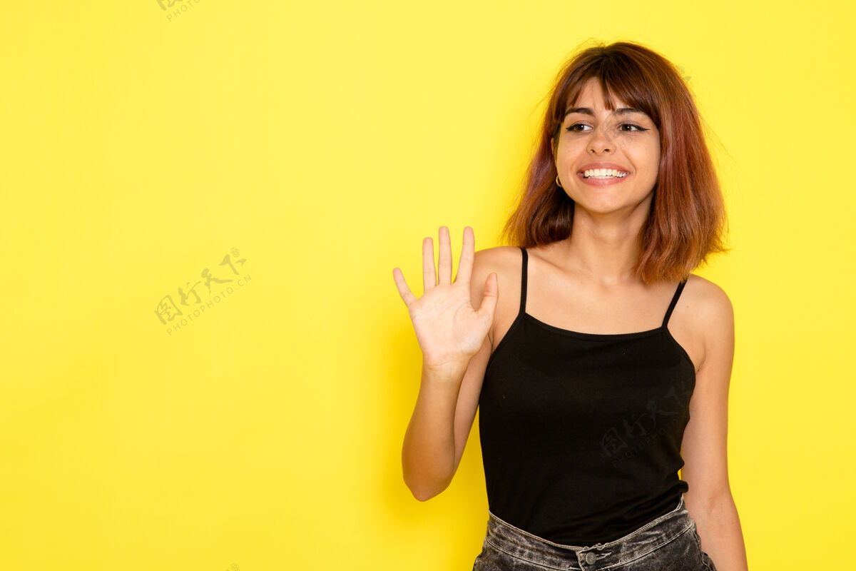 性感身穿黑衬衫的年轻女性在淡黄色的墙上挥舞着她的手年轻情绪光