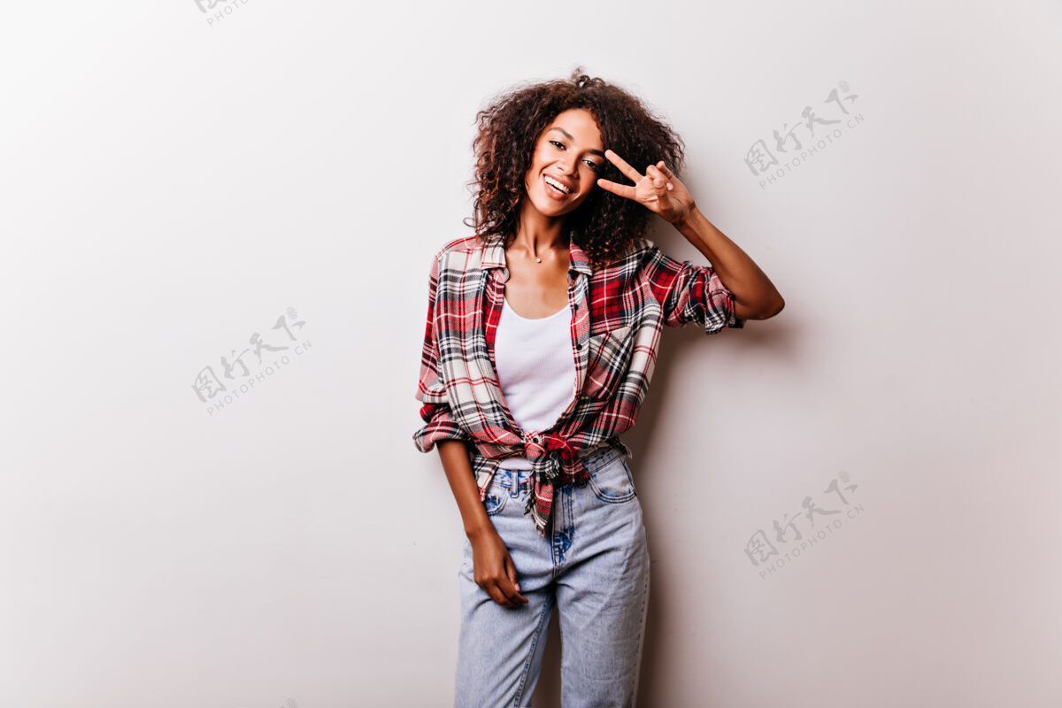 女性可爱的黑色女孩穿着复古牛仔长裤与和平标志合影热情的女模特穿着格子衬衫隔离在白色上配饰休闲快乐