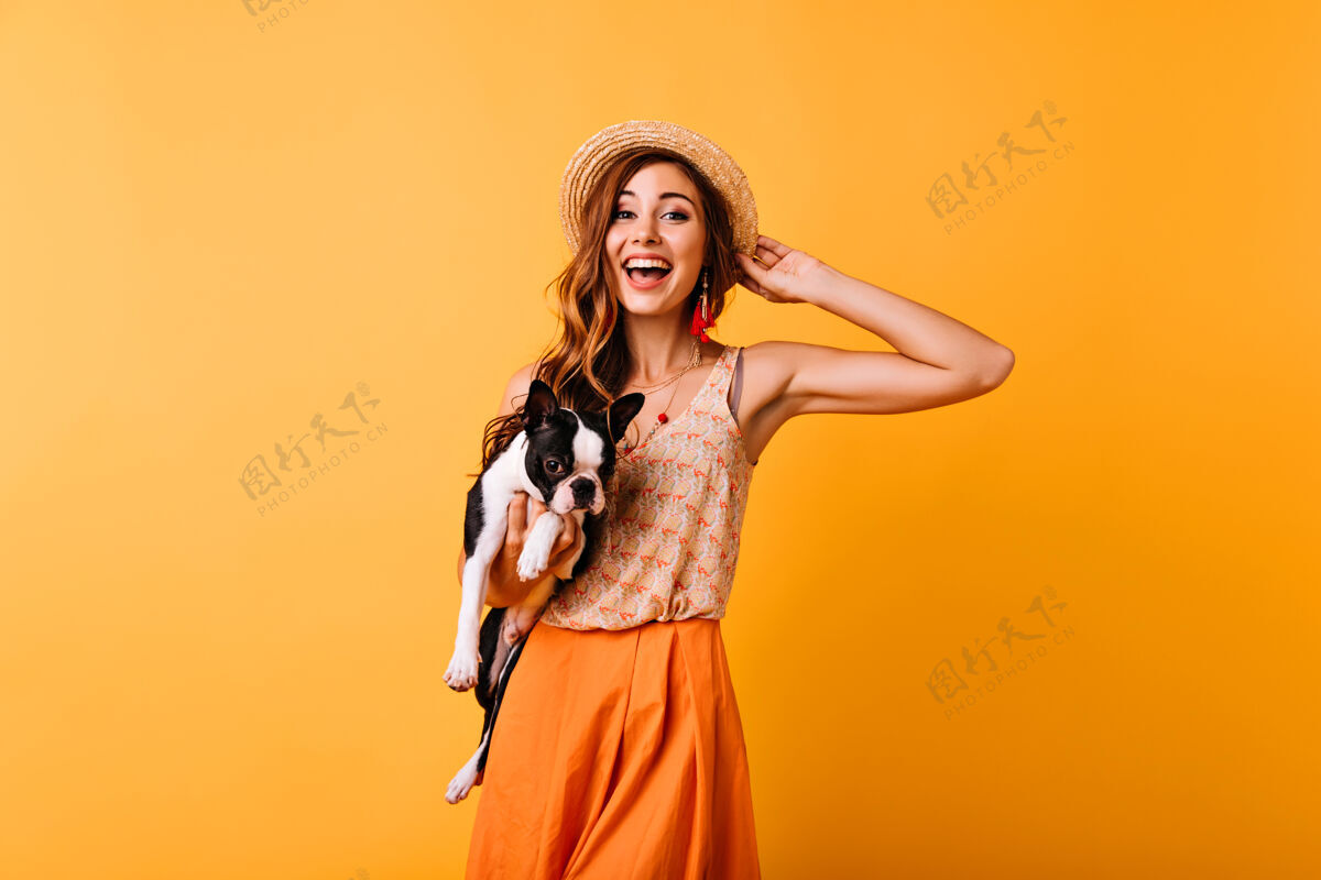 橙色戴着夏日帽子的姜汁女孩在与狗狗的合影中表达着快乐美丽的女孩抱着斗牛犬微笑着友谊朋友成人
