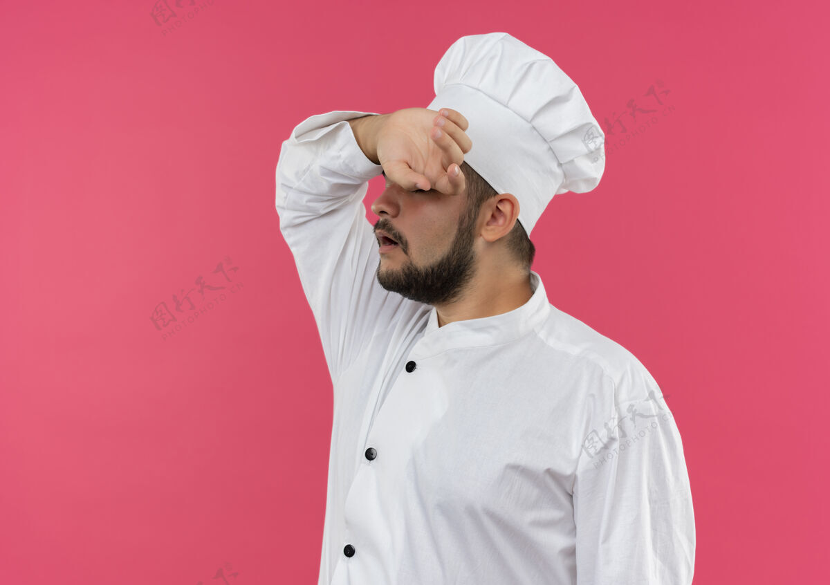 制服疲惫不堪的年轻男厨师身着厨师制服 将手放在隔离在粉色空间的前额上前额厨师厨师