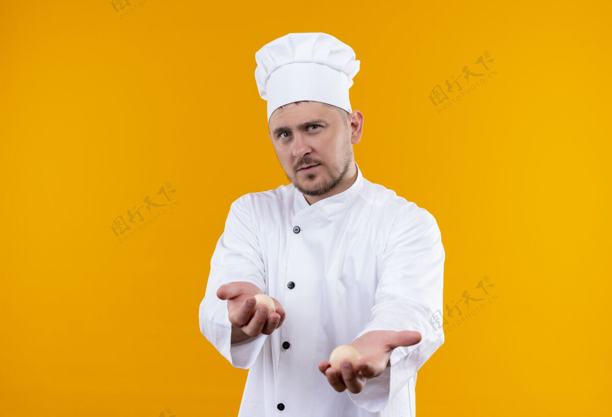 鸡蛋年轻帅气的厨师穿着厨师制服拿着鸡蛋隔离在橙色的空间年轻厨师厨师