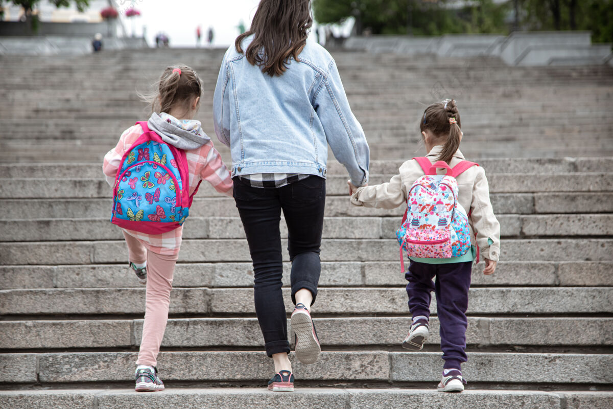 友谊家长和小学生手拉手两个女孩的妈妈背着一个背包开始上课秋天的第一天回来孩子学校