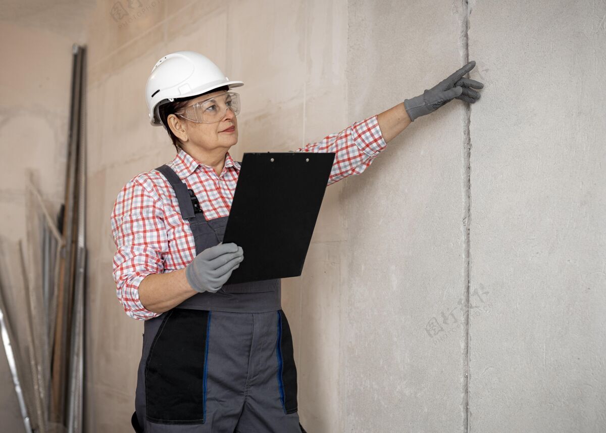安全帽带头盔的女建筑工人用剪贴板检查工作硬劳动者