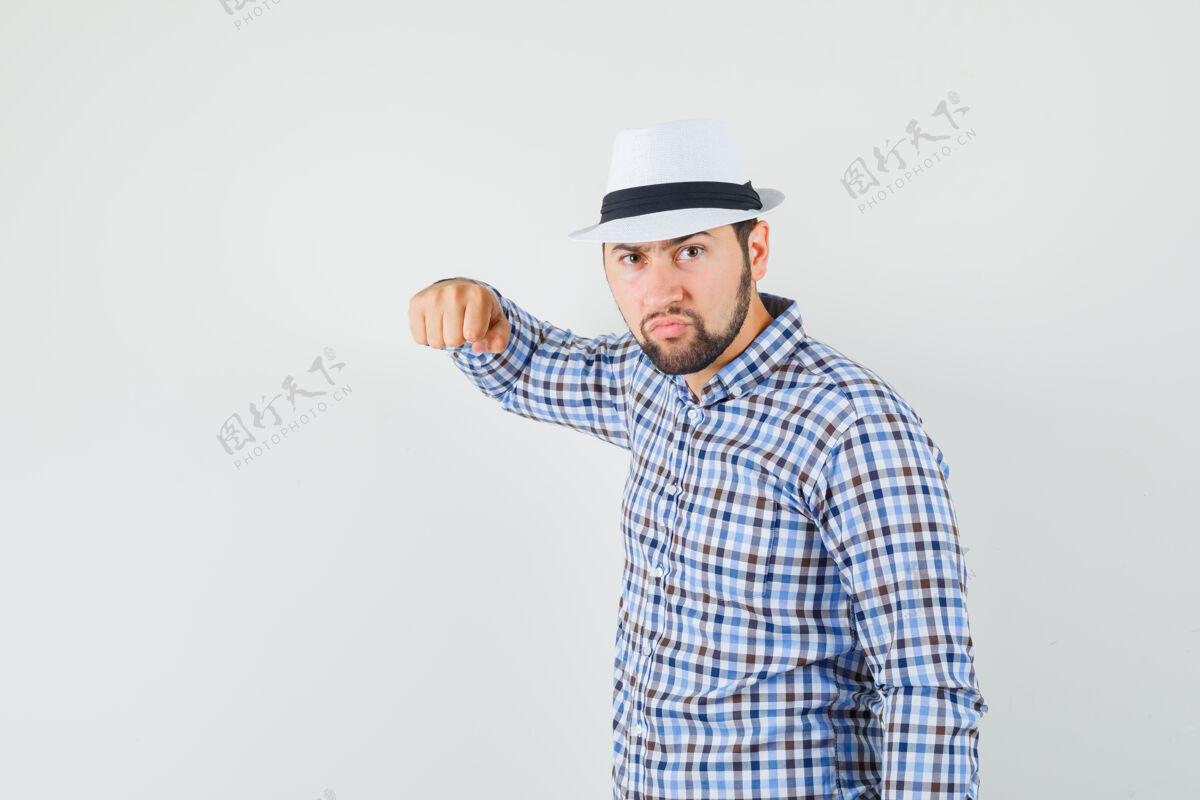 表情年轻的男子威胁与拳头在格子衬衫 帽子和看起来破烂前视图站立严肃自信