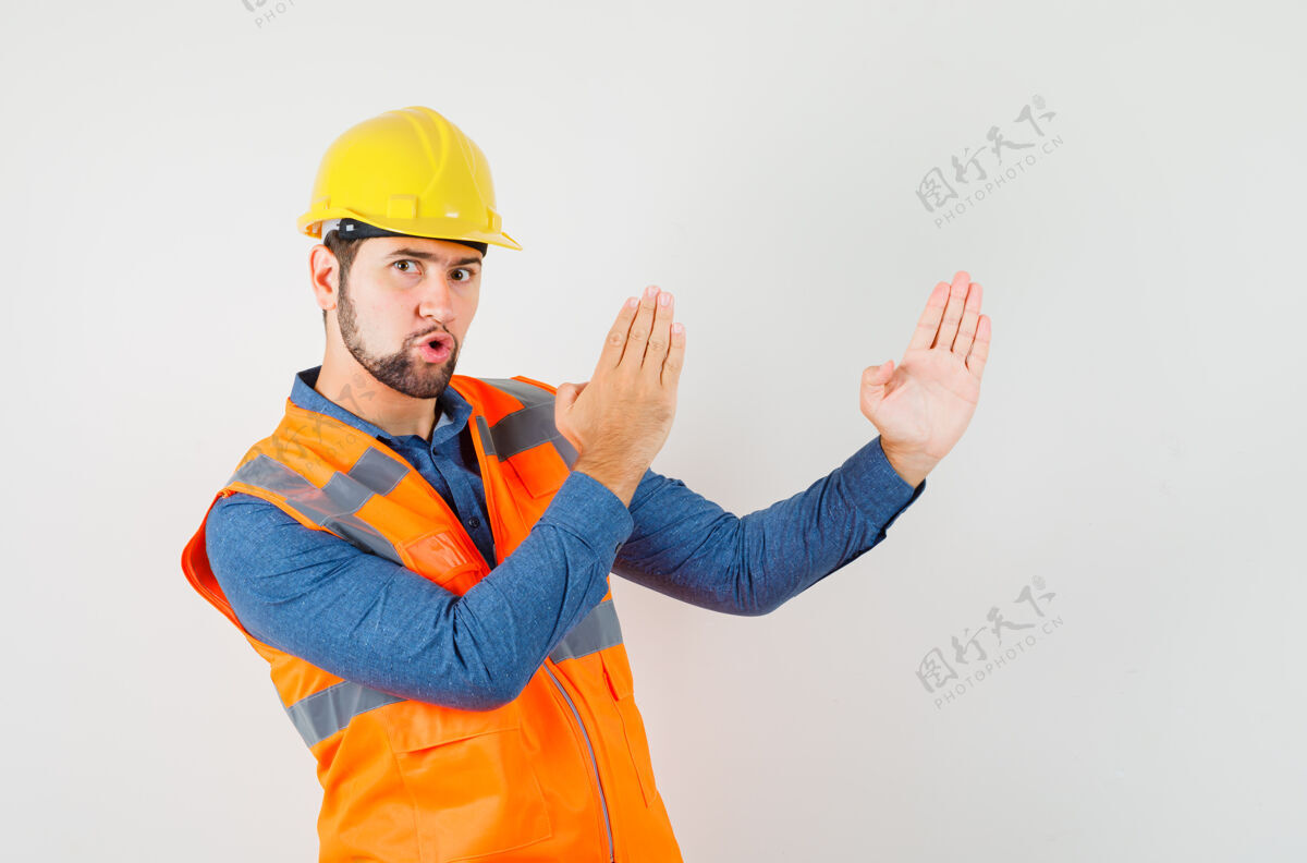 工厂年轻的建筑工人穿着衬衫 背心 头盔显示空手道砍手势和看起来自信 前视图建设者印章工人