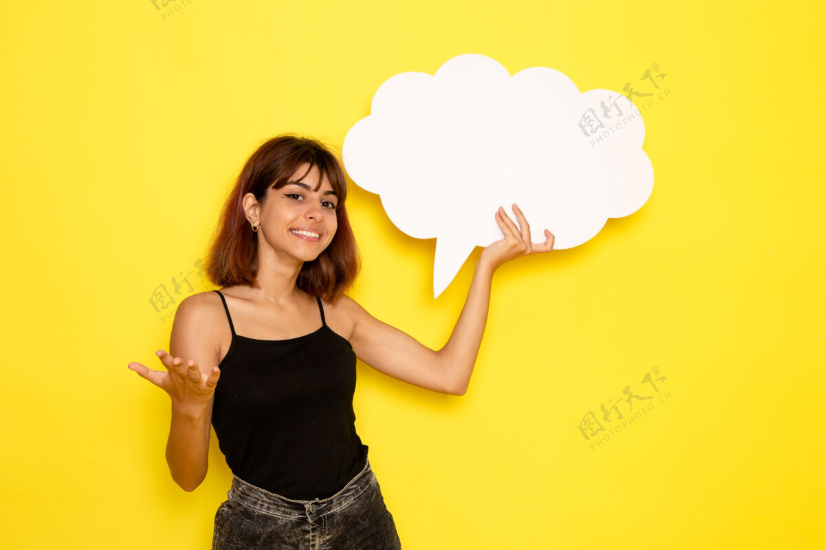 抱着身穿黑色衬衫的年轻女性手持白色大牌子 在浅黄色的墙上微笑漂亮工作衬衫