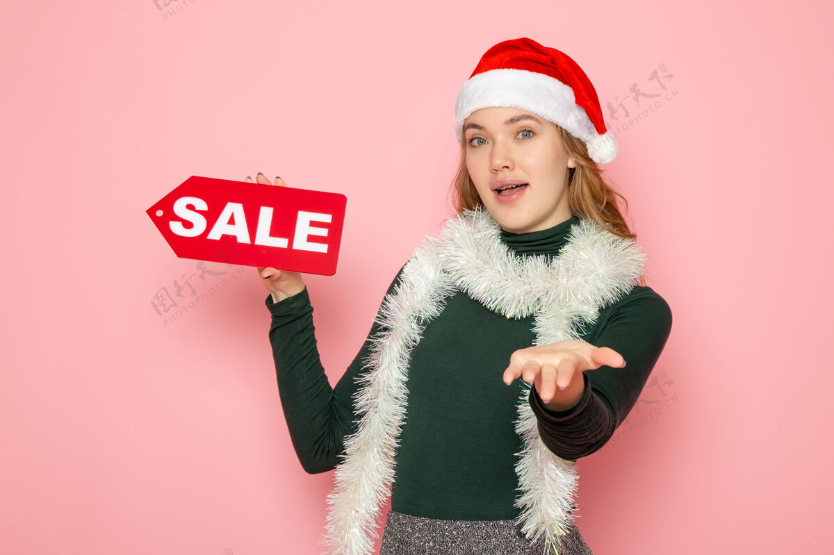 围巾正面图年轻女子手持红色大甩卖写在粉色墙上圣诞假期新年购物时尚感慨肖像帽子羽毛蟒