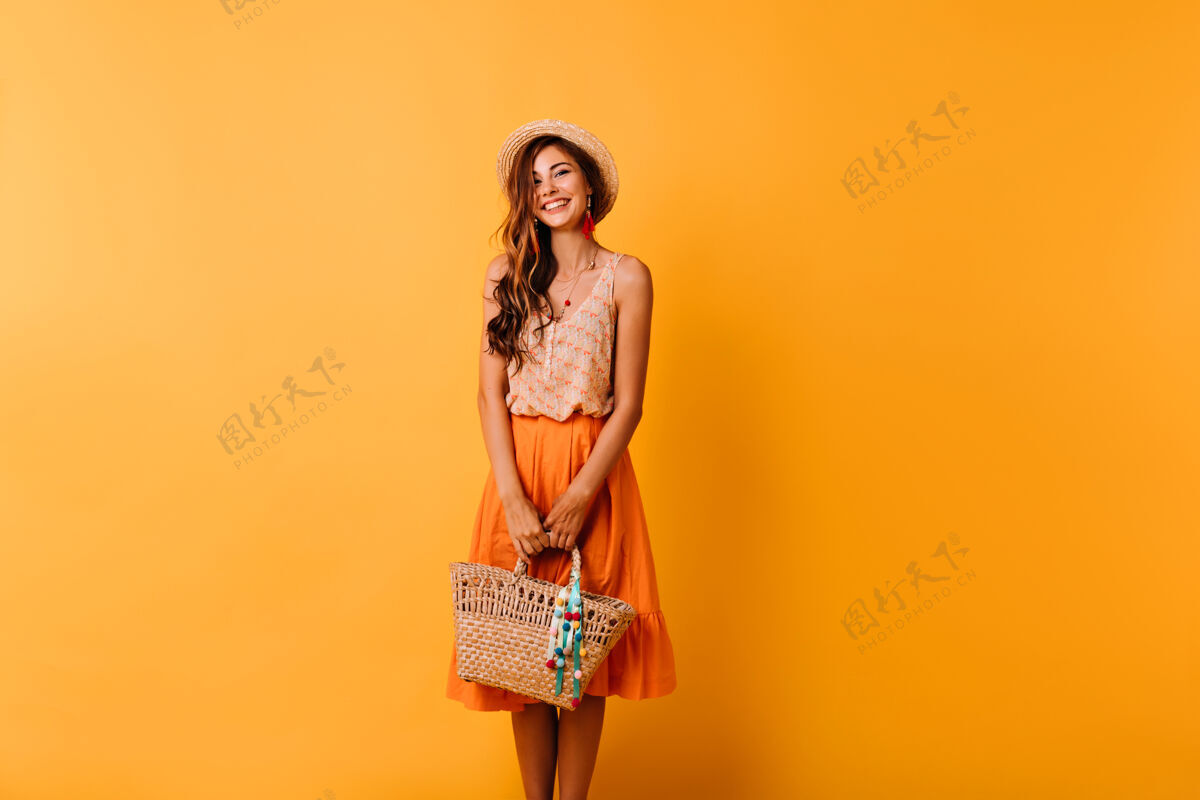 舞蹈穿着夏装准备度假的优雅女人戴草帽的浪漫姜女拿着包在橘子上摆姿势大笑休息乐趣