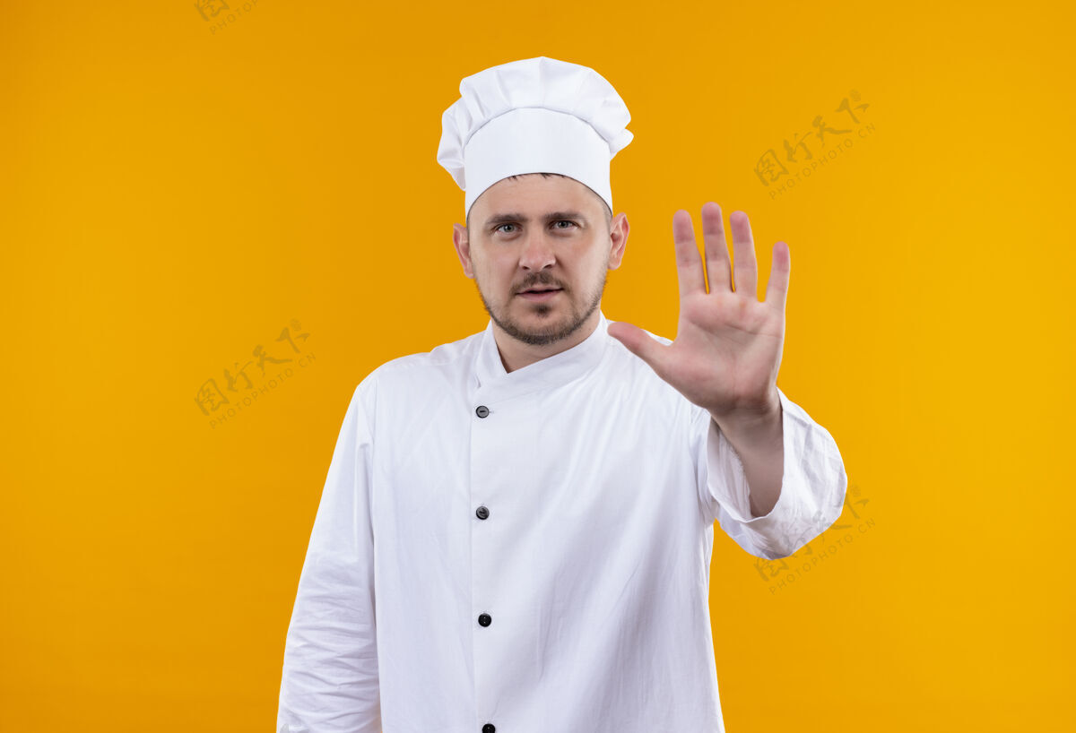 橙色穿着厨师制服的年轻帅哥厨师在橙色的空间里做着手势停下来 看起来很孤立厨师帅气年轻