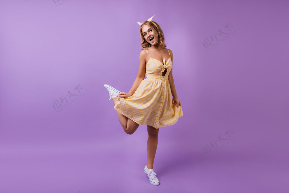 兴奋一只脚站在令人惊艳的棕褐色女孩的全长肖像穿着黄色可爱裙子的积极苗条的女人在紫色上跳舞享受优雅瘦身
