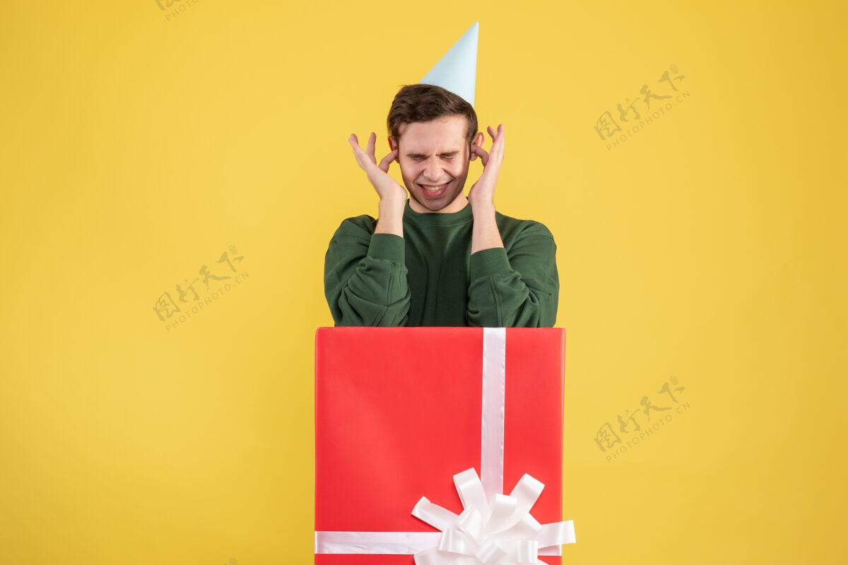 年轻人正面图：年轻人闭上耳朵 手指站在黄色的大礼盒后面微笑购物者礼品盒