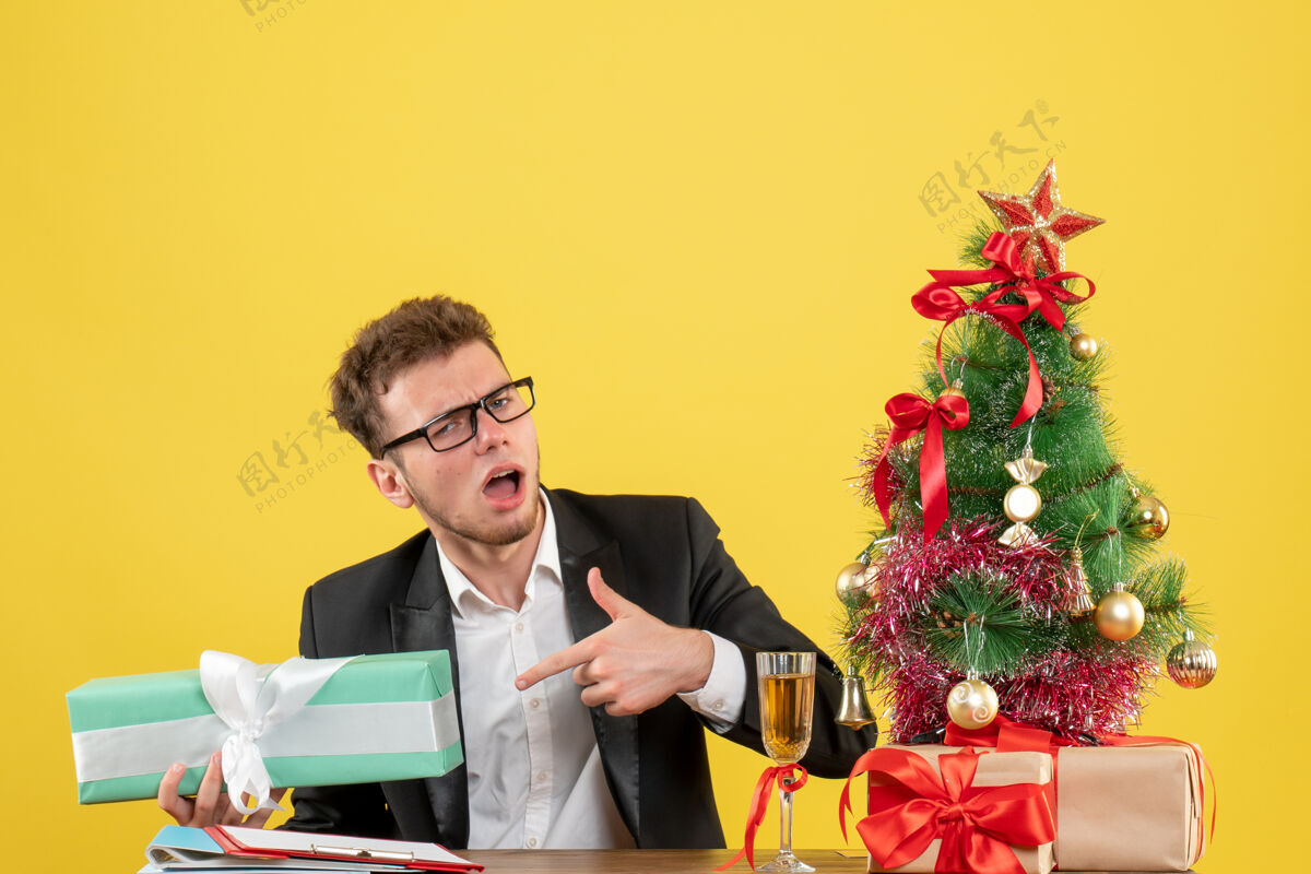 包装正面图：工作场所后面的男工人拿着黄色的蓝色包装的礼物蓝色工作圣诞节