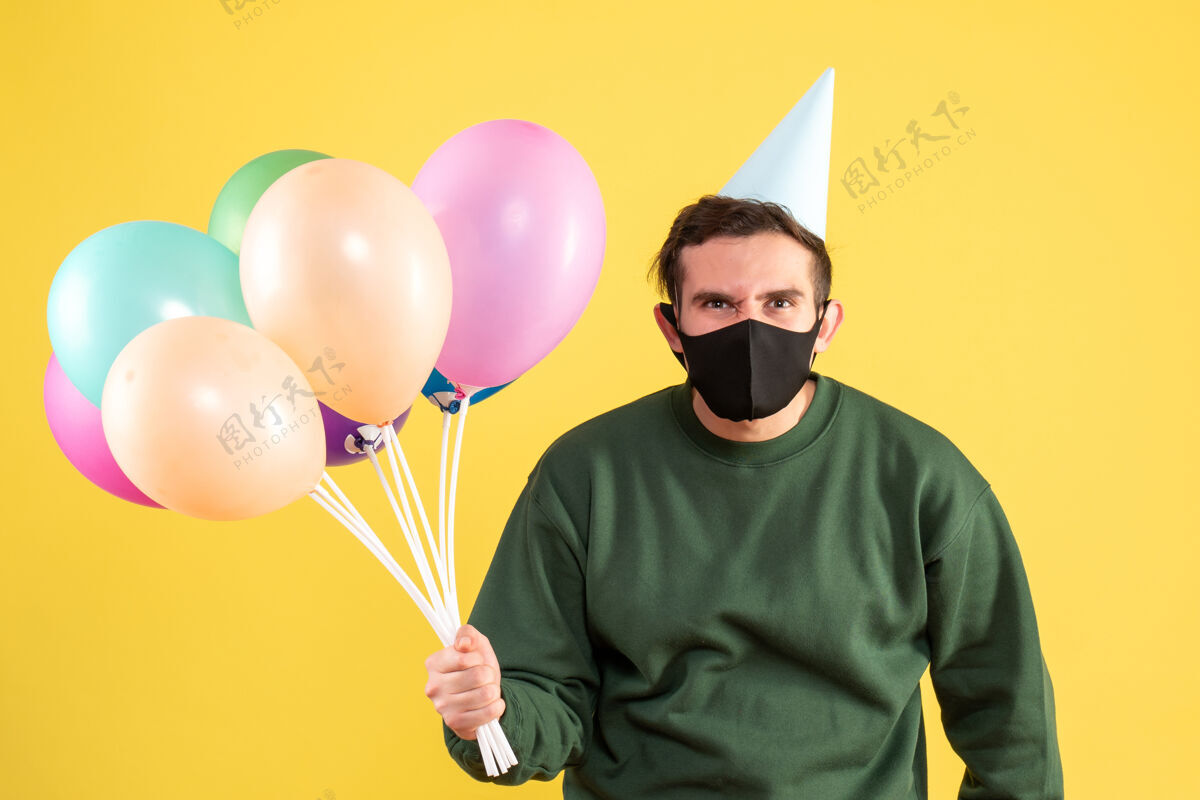 氧气正面图：戴着派对帽 站在黄色地面上的彩色气球的年轻人气球气球乐趣