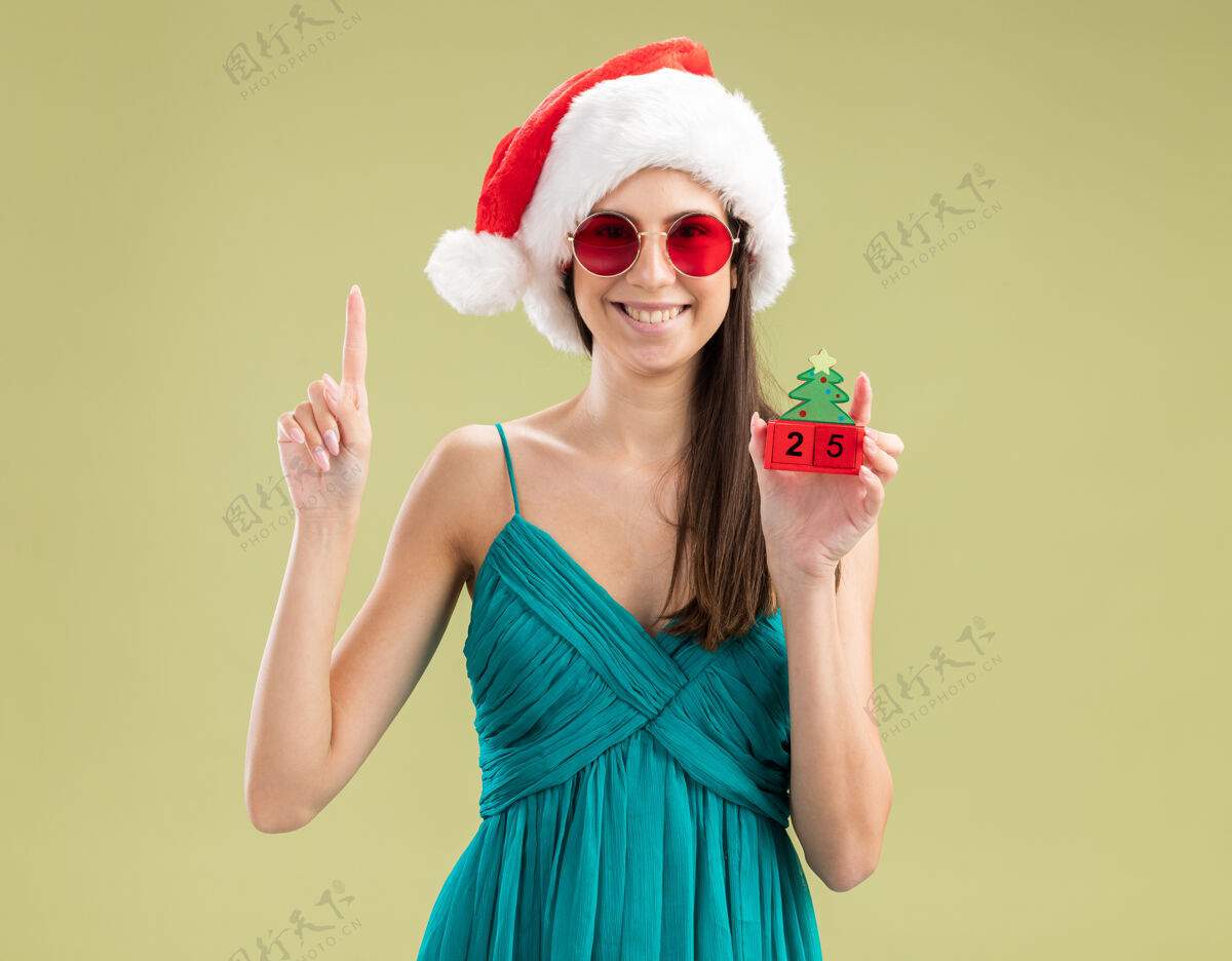 复制戴着太阳眼镜 戴着圣诞帽 拿着圣诞树饰物 面带微笑的白人女孩装饰空间橄榄