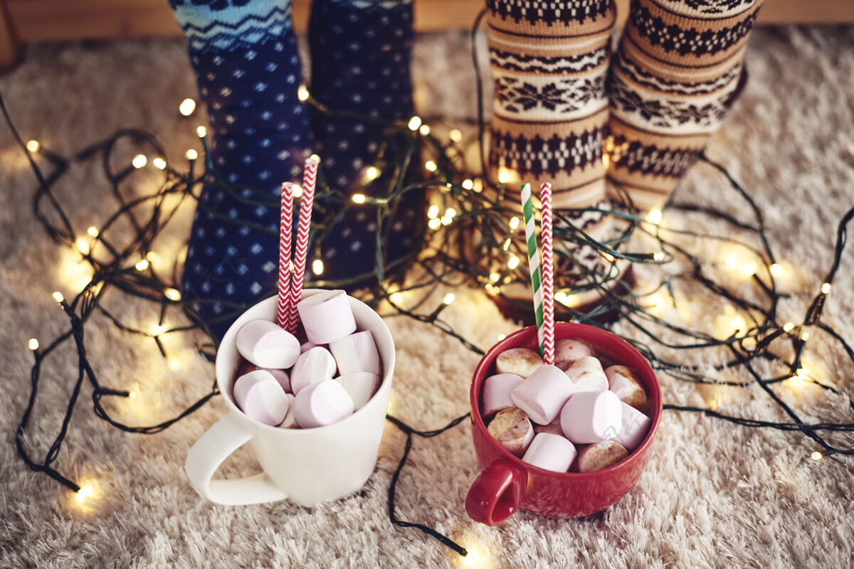 活动两杯热巧克力和棉花糖在地毯上两个人吃热巧克力