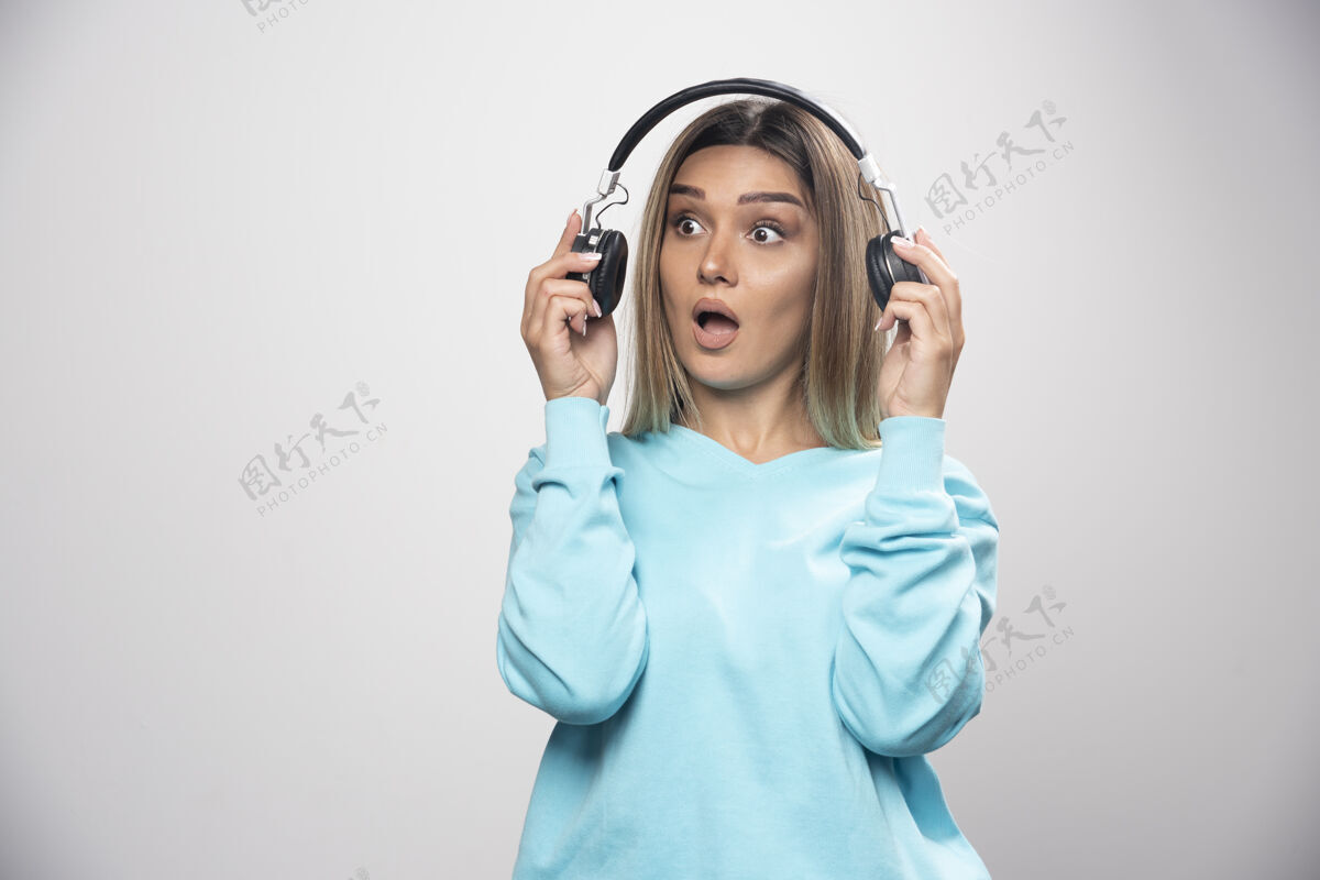 年轻人穿蓝色运动衫的金发女孩拿出耳机听周围的人说话女人音量摆姿势