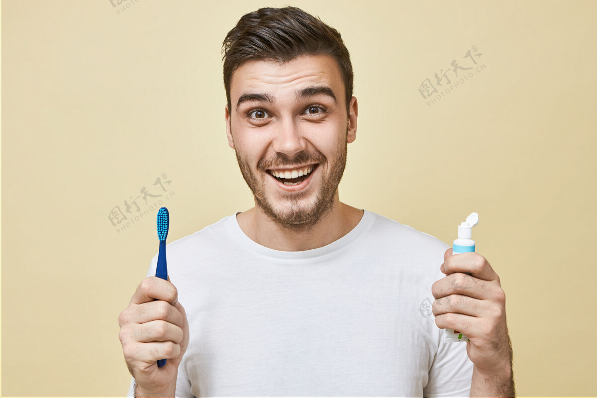 美白精力充沛的积极的年轻人 留着胡茬 拿着牙刷和美白膏 笑容灿烂 牙齿洁白健康的生活习惯 日常生活和牙齿护理年轻牙齿男人