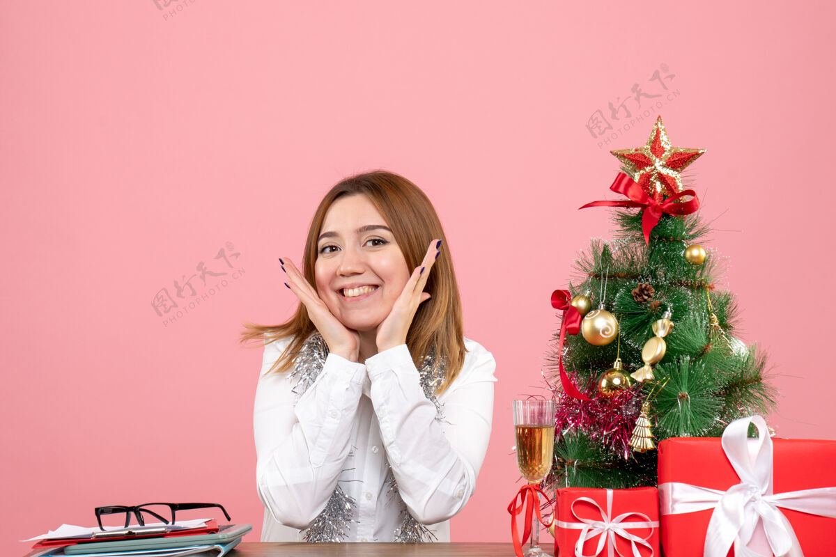 女性女工人坐在桌子后面的正面图 粉色的礼物在微笑桌子礼物工作