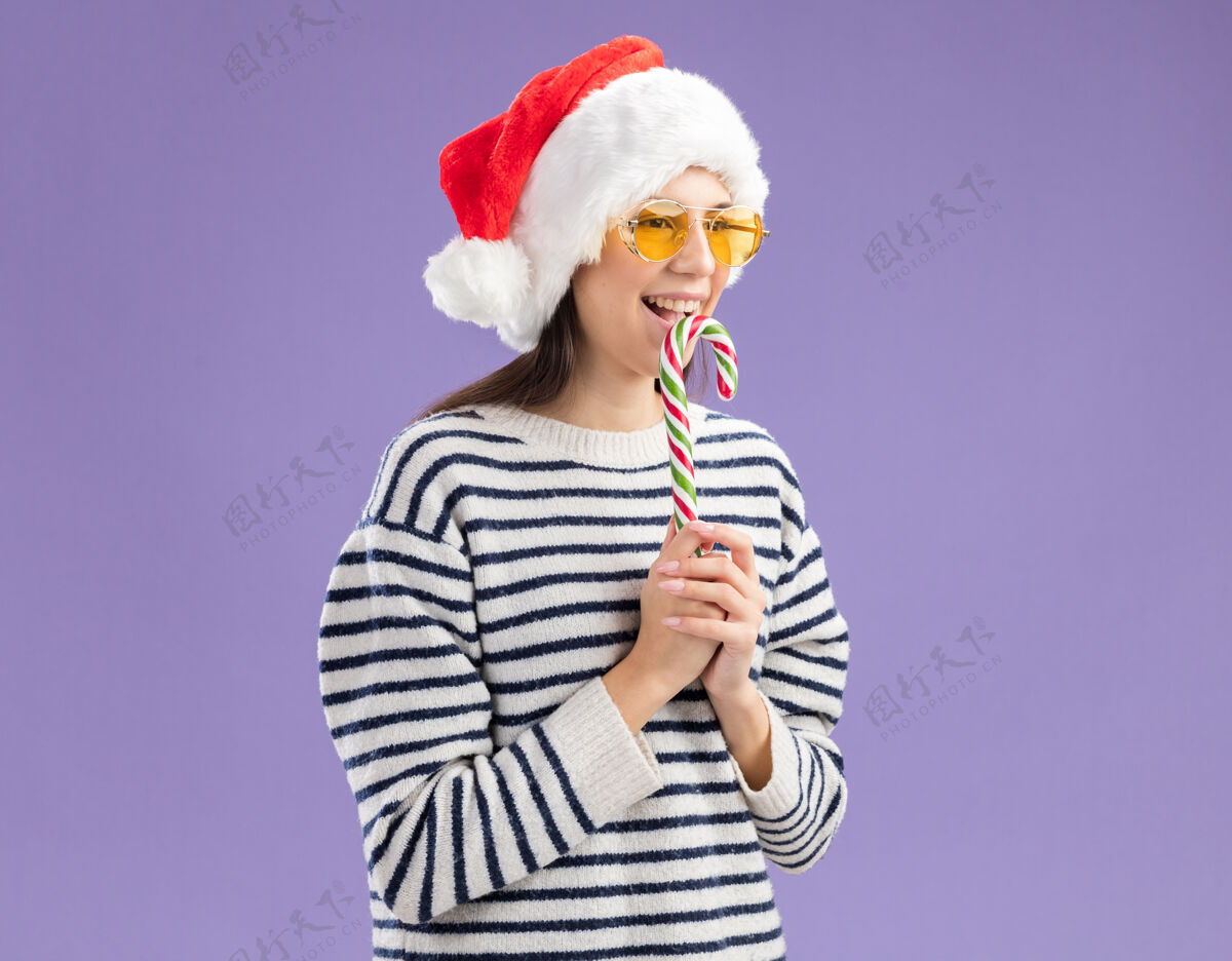 空间快乐的年轻白种女孩戴着太阳眼镜 戴着圣诞帽 手里拿着糖果手杖 看着身边新的边圣诞快乐