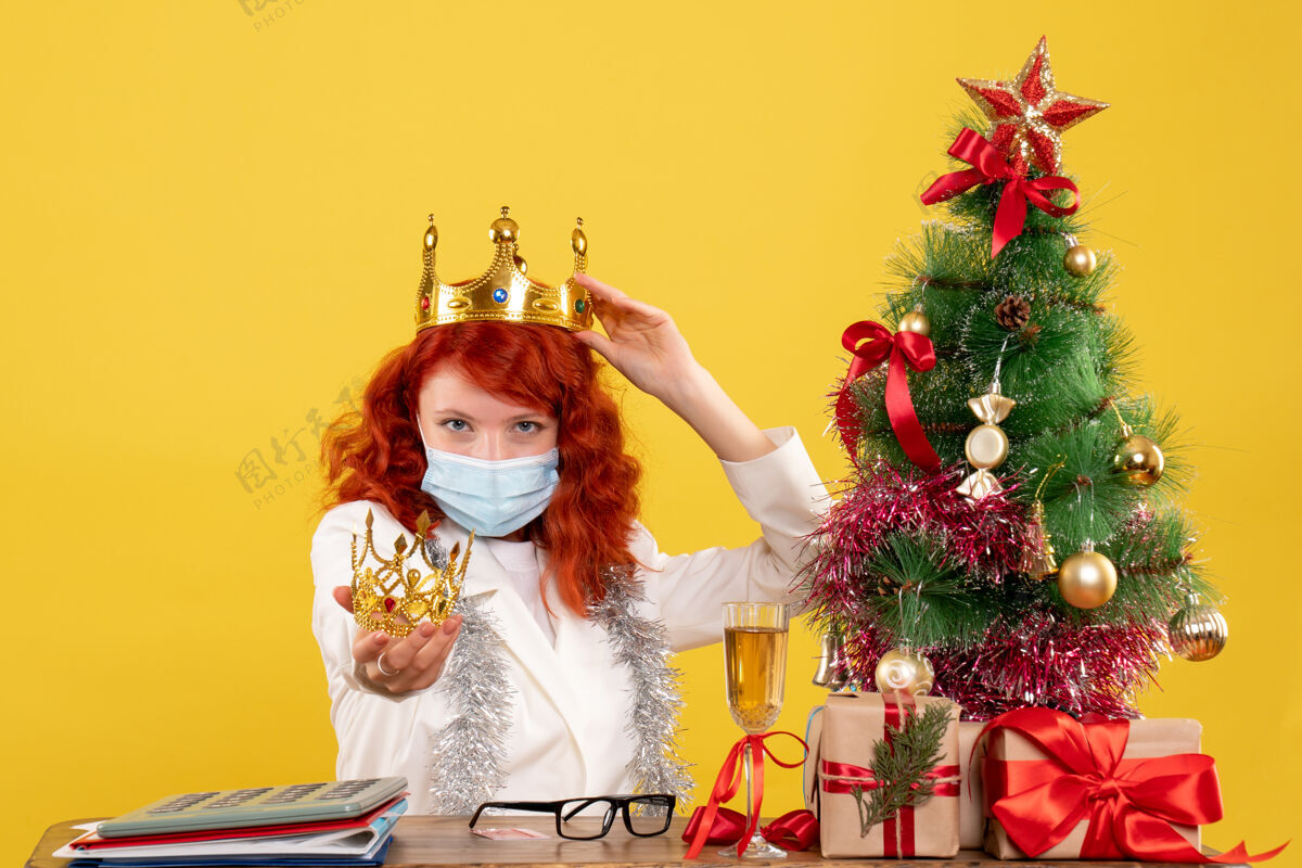 桌子正面图：女医生拿着圣诞礼物坐在黄色的桌子上拿着皇冠肖像抱着皇冠