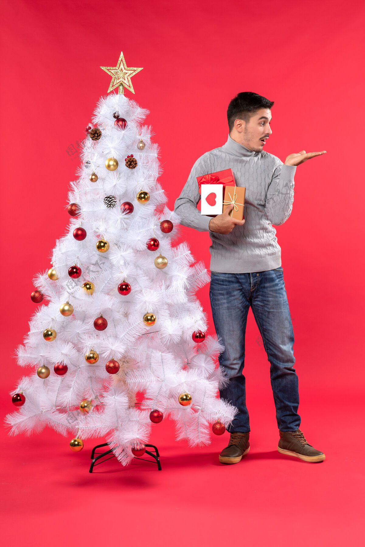 睡衣迷茫的帅哥站在装饰过的白色圣诞树旁 手里拿着他的礼物衣服圣诞树迷糊