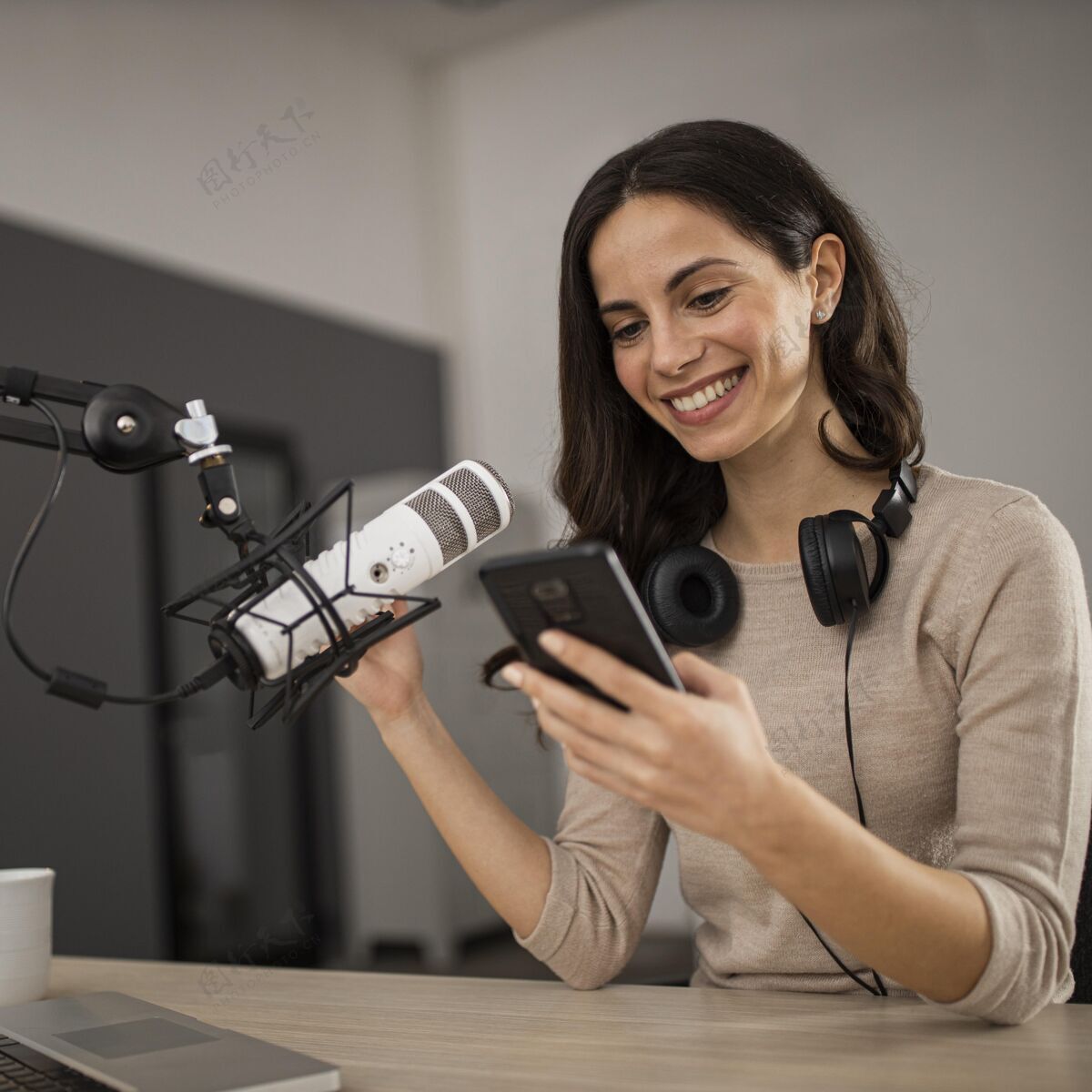 传输微笑的女人 带着智能手机和麦克风在广播室里女士节目播客