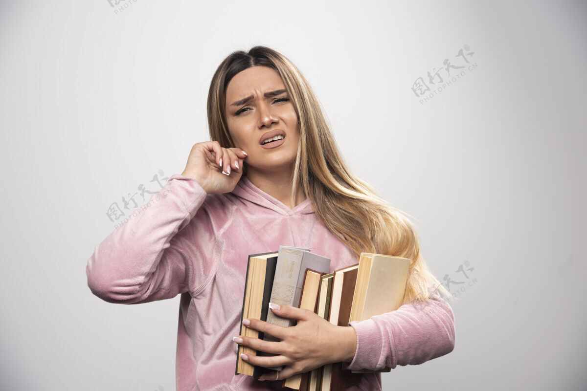 学习穿着粉色衬衫的女孩手里拿着一堆书 觉得很累人类体重疲惫