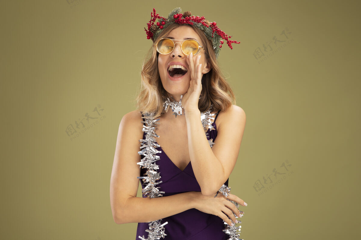 穿着年轻漂亮的女孩穿着紫色的裙子 戴着一副眼镜 脖子上戴着花环和花环 高兴地说有人在橄榄绿的墙上与世隔绝花环花圈礼服