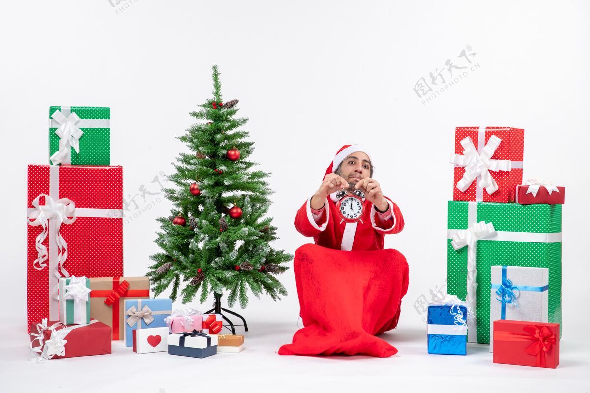 庆祝年轻人坐在地上 在礼物和圣诞树旁展示圣诞钟 庆祝圣诞节装饰礼物年轻人