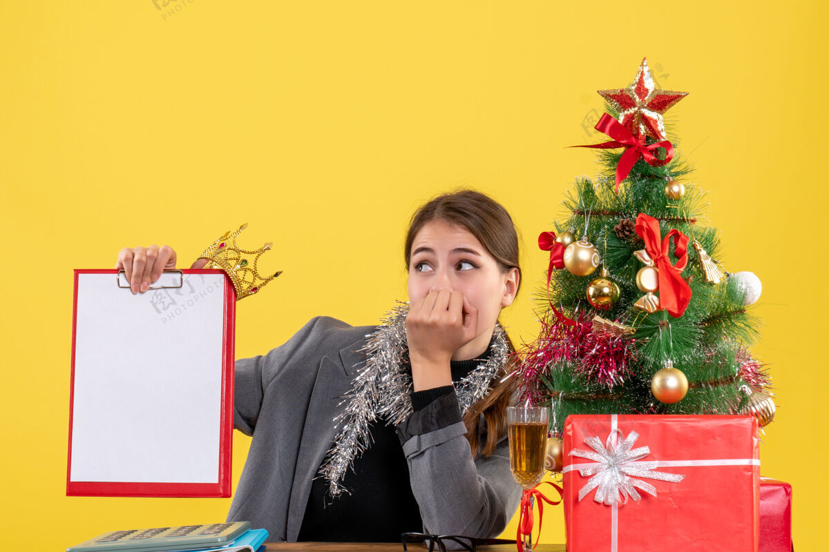 流浪前视图漫步的女孩坐在桌子旁拿着文件 头戴圣诞树和鸡尾酒礼物圣诞节笔记本电脑人