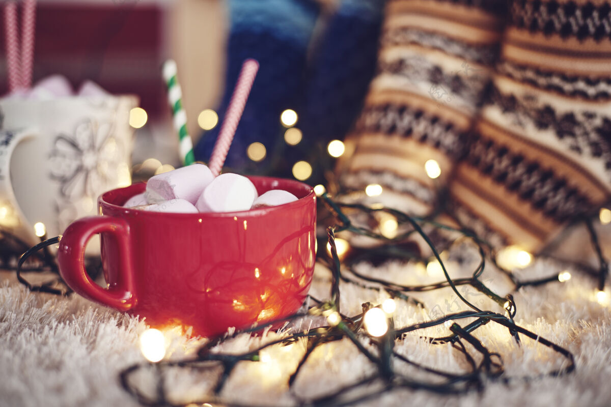 甜点圣诞彩灯和一杯巧克力加棉花糖在地毯上放松棉花糖放松