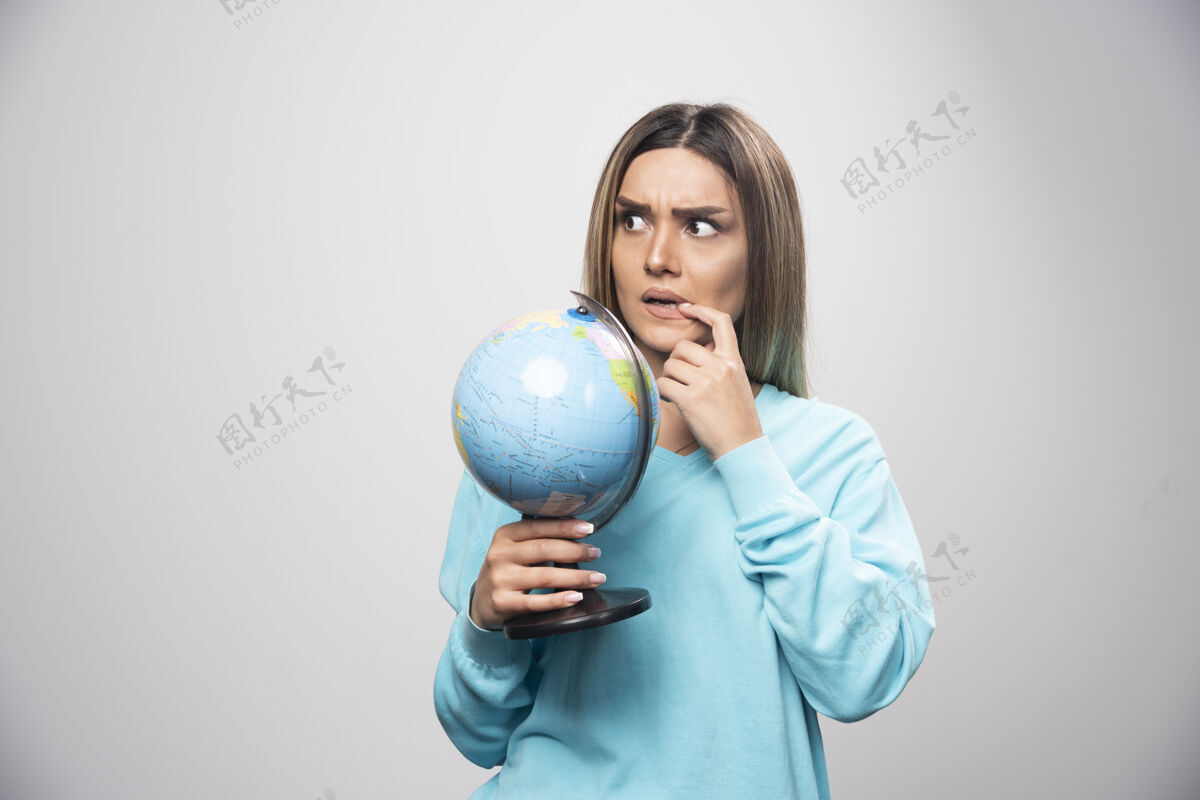 教育穿着蓝色运动衫的金发女孩手里拿着一个地球仪 仔细地思考 试图记住年轻人成人目的地
