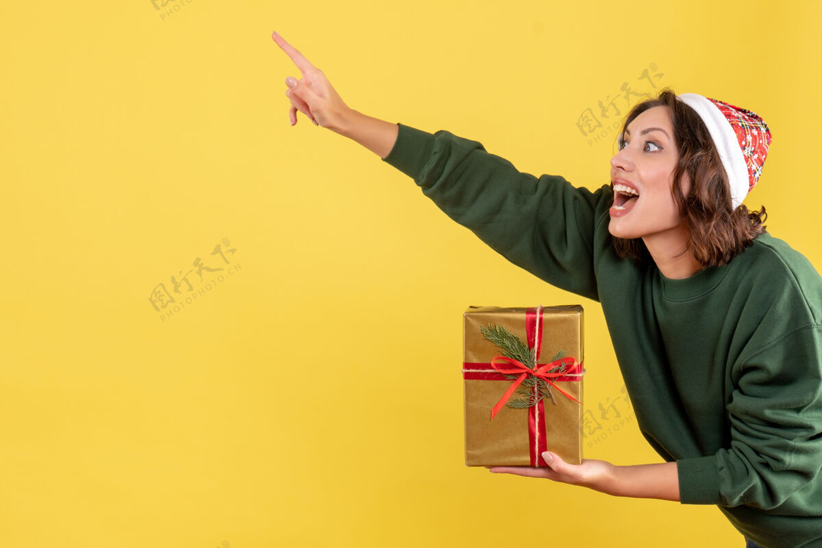 病毒黄色墙上拿着小圣诞礼物的年轻女子的正视图小女人抱着