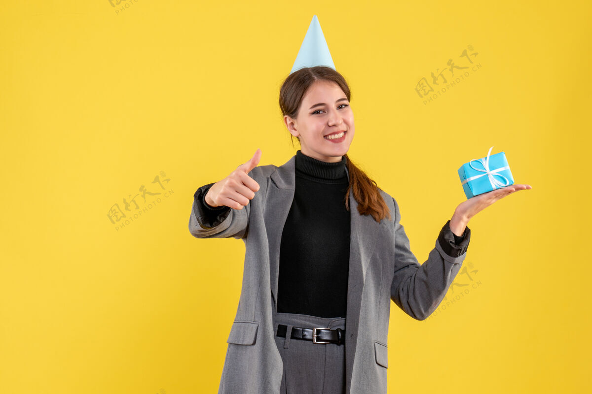 帽子前视图高兴的女孩与党的帽子举行她的礼物制作拇指向上的标志高兴的女孩制造礼物