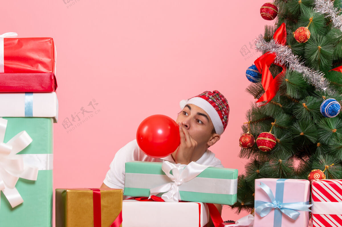 盒子一个年轻人庆祝圣诞礼物周围的粉红色墙上的前视图快乐圣诞节庆祝