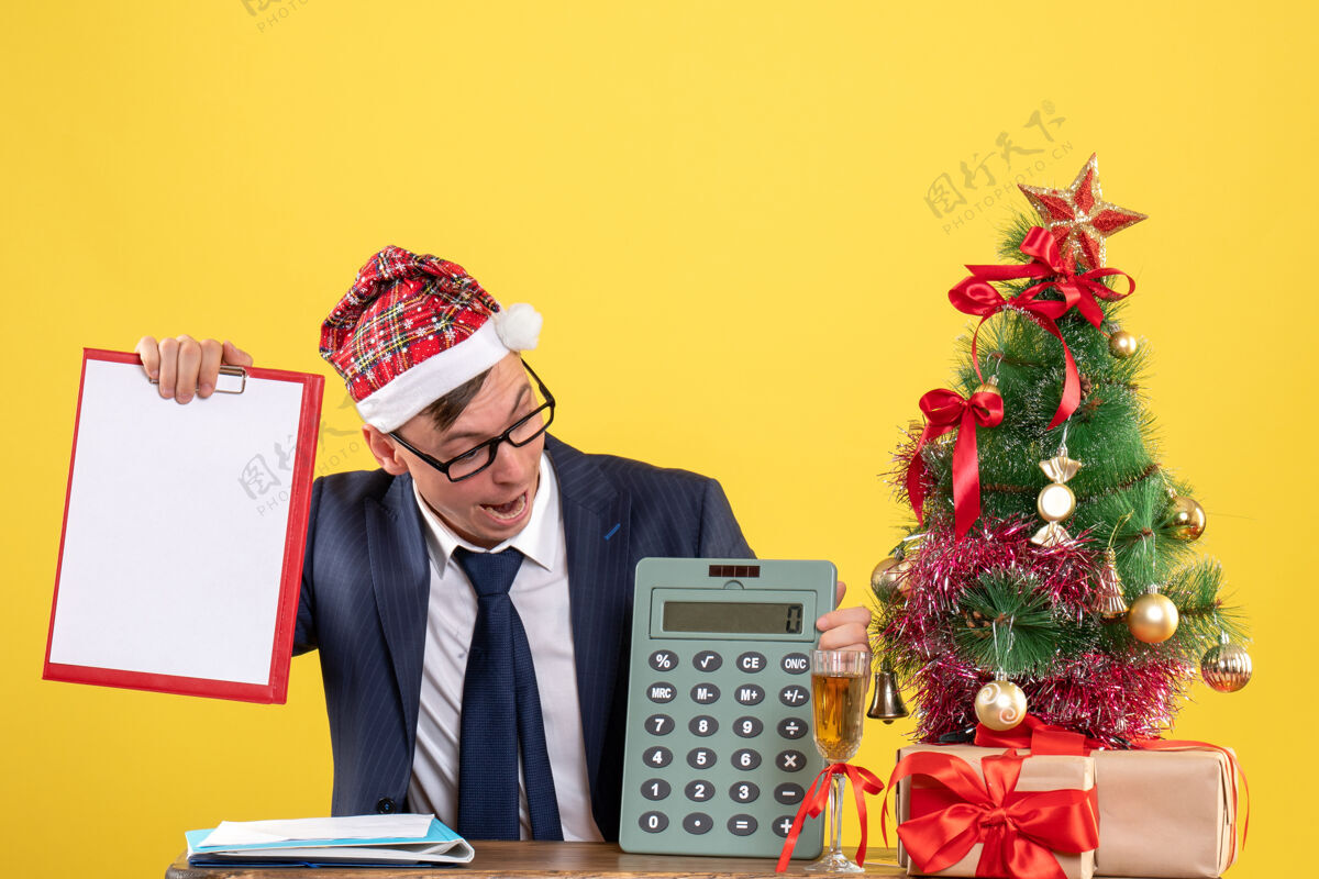 秘书商务人士坐在圣诞树旁的桌子旁看计算器 黄色的礼物办公室西装商务人士