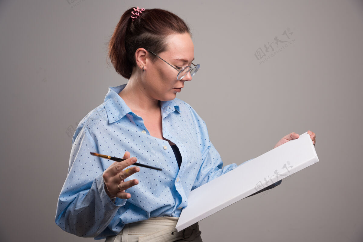休闲女人看着空画布和灰色背景上的画笔女人情感列表