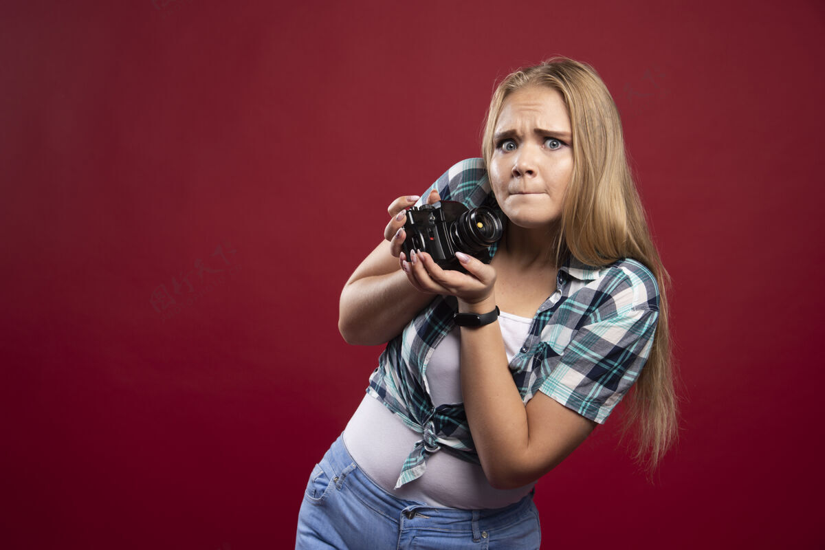 工人年轻的金发女郎拿着专业相机拍照 不知道怎么用吓坏了人女人