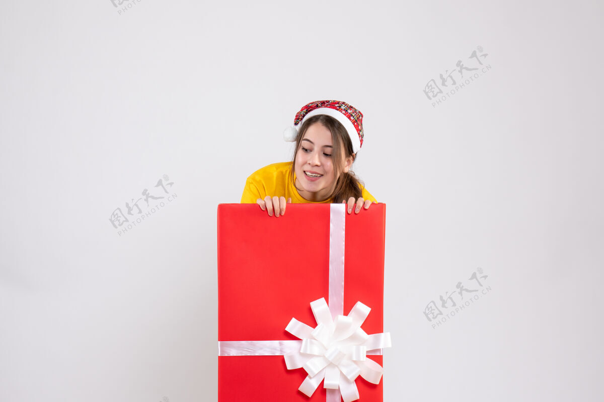 圣诞节戴着圣诞帽的窥探女孩看着白色大圣诞礼物后面的东西女孩礼物站着的