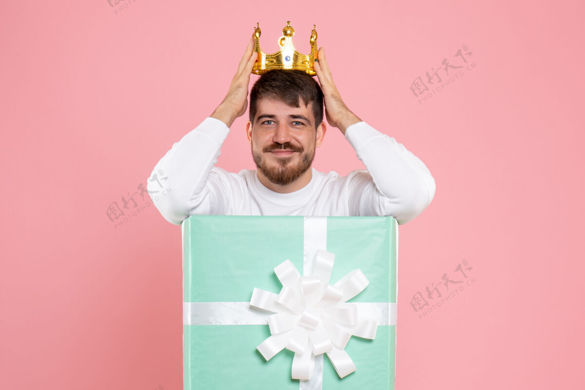 前面粉红色墙上戴着王冠的礼物盒内年轻人的正面图年轻购物情感