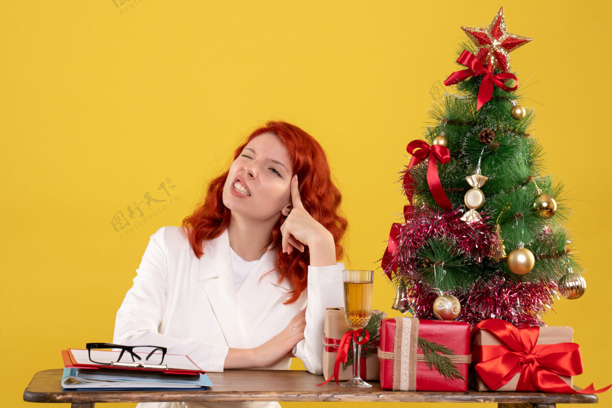 圣诞节女工人坐在桌子后面 手里拿着圣诞树和黄色的礼物坐着主任小孩