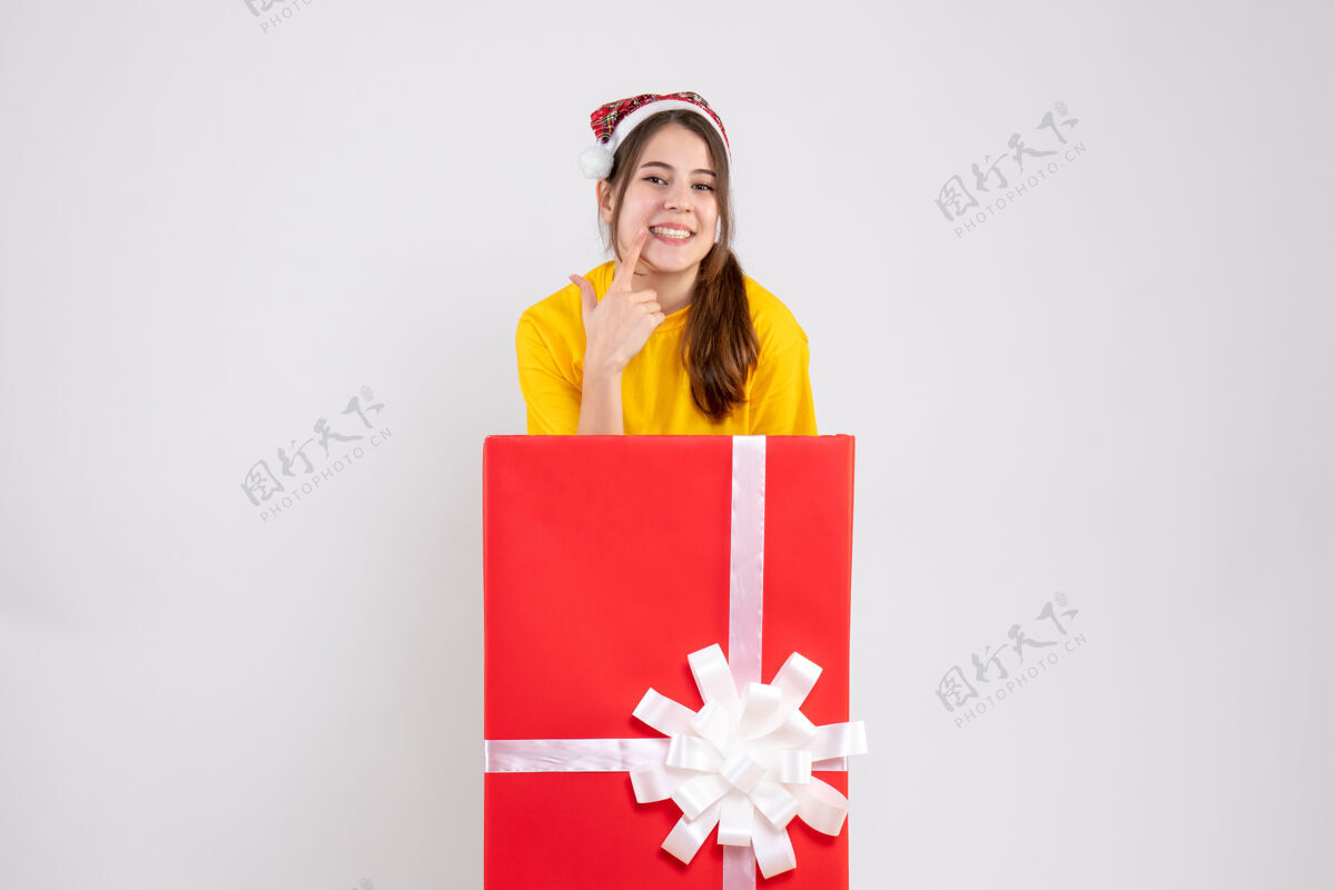 圣诞节戴着圣诞帽的快乐女孩站在白色圣诞礼物后面露出微笑礼物购物帽子