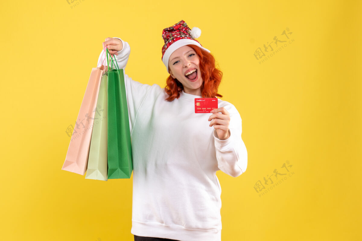 微笑黄色墙壁上拿着购物袋和银行卡的年轻女子的正视图卡微笑银行