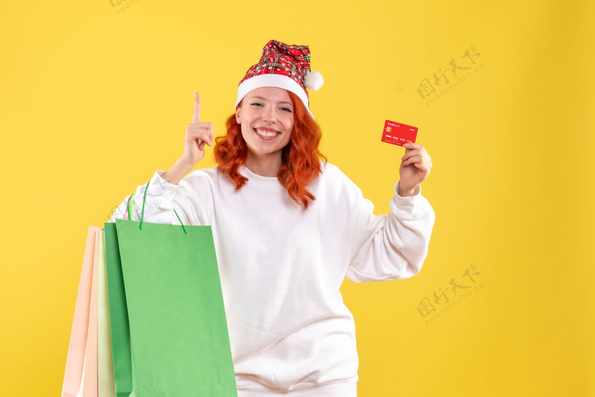 人黄墙上拿着购物包和银行卡的年轻女子的正视图前面购物年轻
