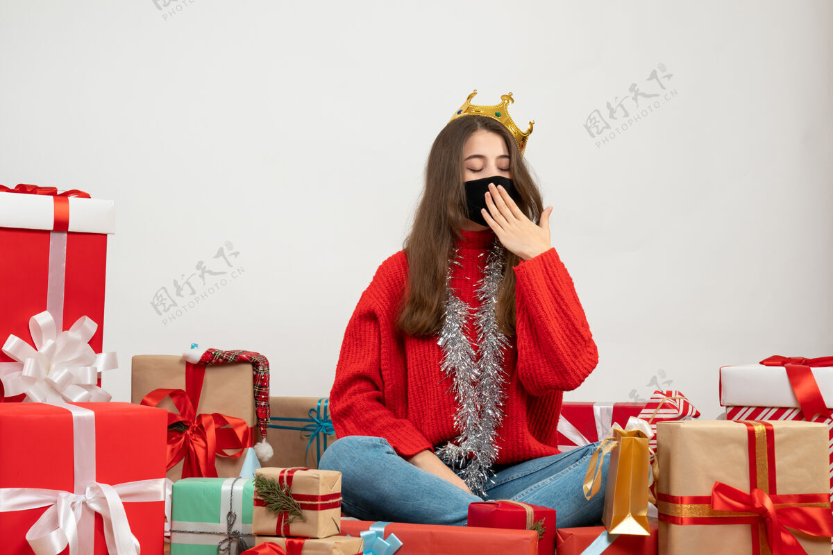 年轻穿着红色毛衣的困倦女孩围坐在礼物旁边 白色的面具上戴着黑色的面具漂亮面具时尚