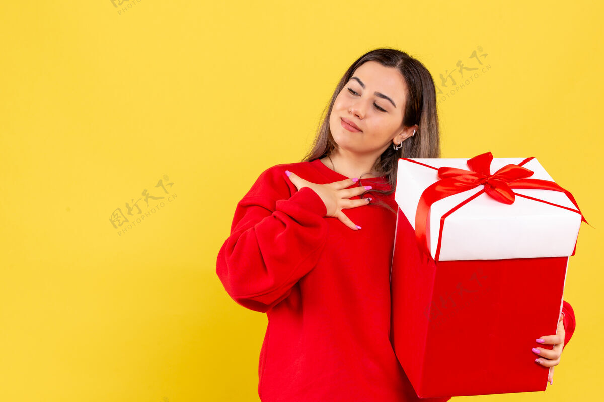 快乐黄色墙上手持圣诞礼物的年轻女子的正视图十二月节日微笑