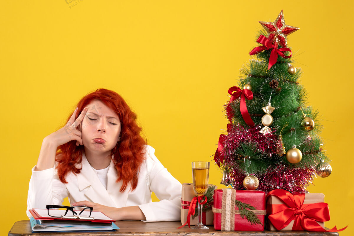 整理女工人坐在桌子后面 手里拿着圣诞礼物和黄色的圣诞树办公室女黄色