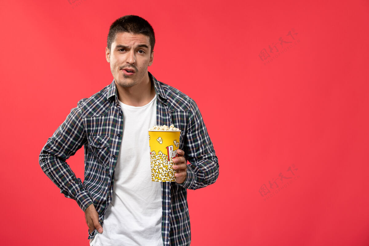 男人正面图年轻男子手持爆米花包 在淡红墙电影院摆姿势摆姿势西装包装