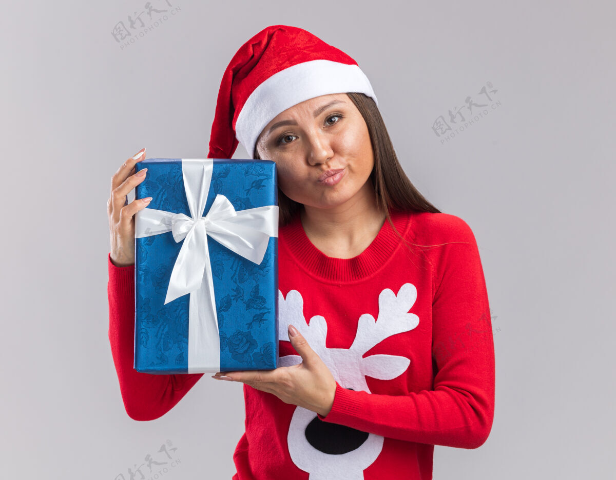 帽子未出租的年轻亚洲女孩戴着圣诞帽和毛衣拿着礼品盒隔离在白色背景上年轻人毛衣礼物